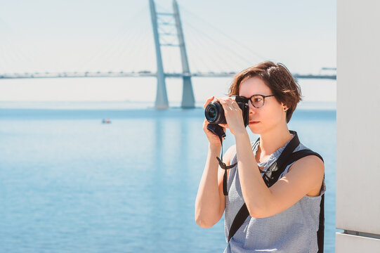 A tourist girl takes photos against the background of the bridge and the sea. Photographer while shooting a landscape