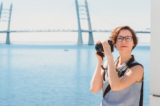 A tourist girl takes photos and smiles against the background of the bridge and the sea. Photographer while shooting a landscape