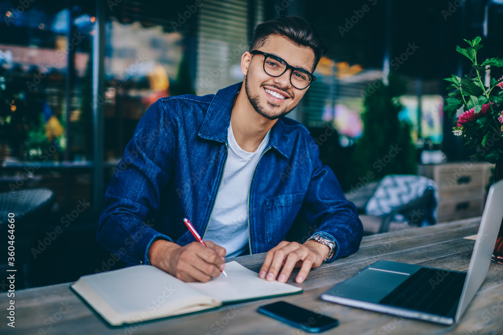 Poster portrait of skilled caucasian male student writing in notepad enjoying learning using laptop compute