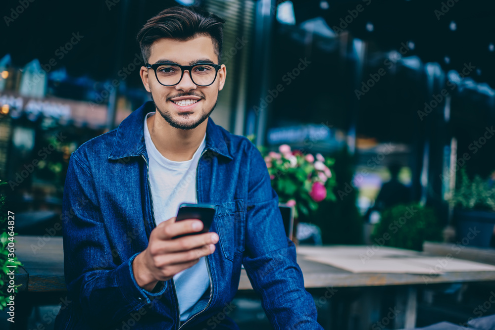 Aufkleber portrait of bearded hipster guy in spectacles using mobile phone for chatting and networking spendin