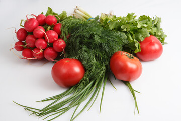 close up top view shot of a vegetable composition consisting of a bunch of radish, dill, parsley, green onions and ripe red tomatoes on a white background