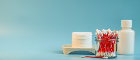 Ear sticks in a glass container, white cotton pads and cleanser on a blue background. Concept of hygiene and skin care. Place to copy