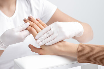 Human hands in protective gloves holding female fingers with beige polish on nails in beauty salon