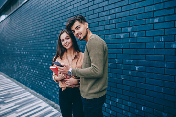 Portrait of young male and female students checking news from networks using smartphone together,...