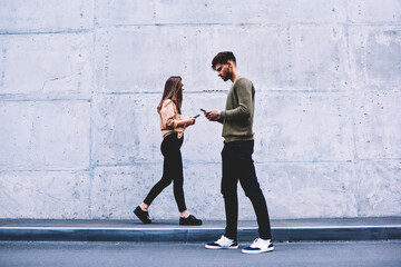 Fototapeta na wymiar Male and female hipsters walking on grey wall background ignoring each other preferring social networks,students chatting online instead of communicating in real life strolling pon publicity area