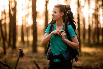 view of smiling young woman with sport backpack which walking in forest