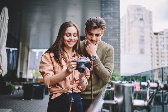 Young couple viewing pictures on camera spending free time on hobby together outdoors, cheerful hipster girl showing to her boyfriend pictures on equipment enjoying leisure and date on urban setting