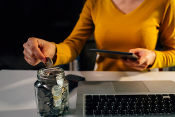 saving money with hand putting coins in jug glass and calculator to calculate budget concept finance and accounting