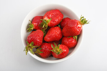 isolated close up top view shot of a bunch of whole vibrant red strawberries in a bowl on a white background