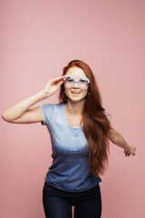 A cheerful girl in blue round sunglasses rejoices and dances in the studio on a pink background