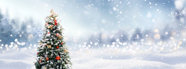Beautiful Festive Christmas snowy background with holiday lights. Christmas tree decorated with red balls and knitted toys in forest in snowdrifts in snowfall on nature outdoors, panoramа, copy space. - Powered by Adobe