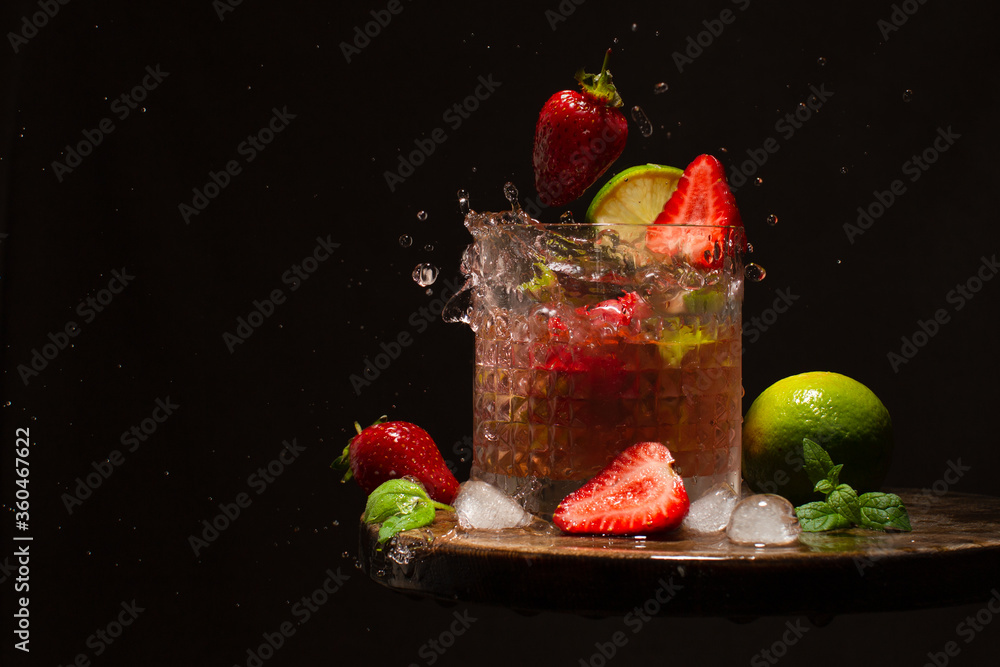 Wall mural Refreshing cocktail with strawberry,lime,mint leaves,water and ice cubes on wooden table.Splash of strawberry cocktail.