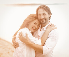 Beautiful couple stand embracing against sea or ocean background. Smiling man and woman in white clothes hugging each other. Tinted image.