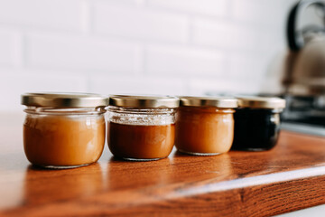 Little honey cans on the wooden table. Honey variety cans in a row. Bright kitchen interior. Wooden complete kitchen with gas oven