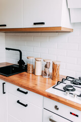 Glass jars with grain in kitchen. Bright kitchen interior. White modern dining room. Wooden complete kitchen with gas oven