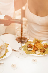 Red wine is poured into glass against background of woman in summer white dress with deep neckline. Close up shot. Tinted image.
