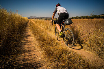 A man riding a gravel bike on Spanish farm tracks through fields of yellow grass