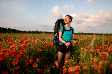 front view of smiling female tourist who stands on field of red poppies.