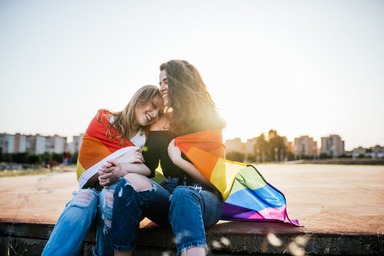Two young girls sitting close at sunset with a rainbow flag of LGBT pride