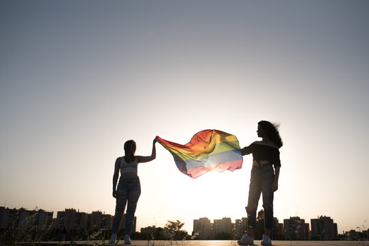 silhouette of two girls waving a rainbow flag of LGBT gay pride in the wind at sunset. Vertical photography