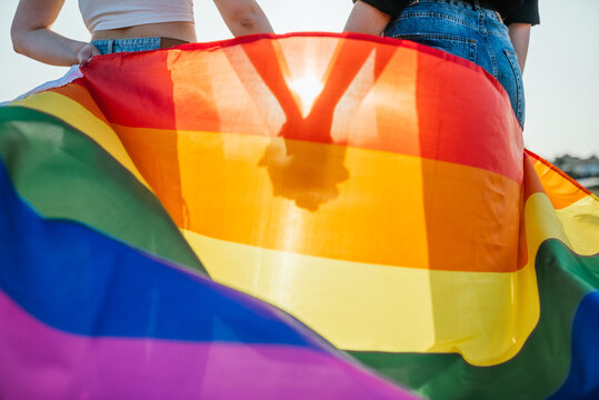 silhouette of two girls holding hands at sunset with a rainbow flag of LGBT gay pride.