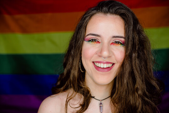 Portrait of young girl smiling with colorful makeup against the background of the rainbow flag of gay pride