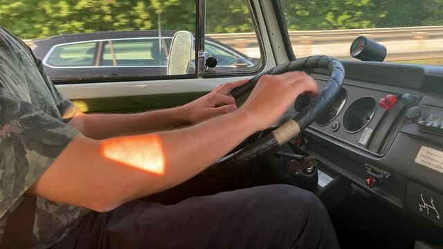 Young man driving an old T2 vanagon on a highway in the evening sun.
