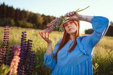 Girl in a hat looks directly at the camera and holds wildflowers flowers in front of her face