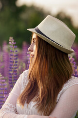 A girl with her hair in a lupine field looks at the setting sun and her profile is highlighted by the sun.