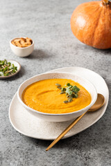 Pumpkin soup with cream garnish microgreens on grey background. Vertical format. Close up.