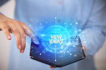 Businessman holding a foldable smartphone with NEW IDEAS inscription, new business concept