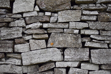 Background of dry stone wall at Monsal Dale in the Peak District National Park. Angular stones with visible sediments. Xanthoria lichen both yellow and sun bleached on the surface.