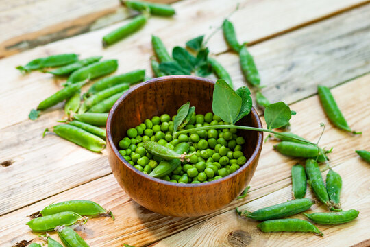closeup green peas in brown dish, on wooden table.