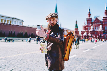 Smiling hipster with smartphone walking on square