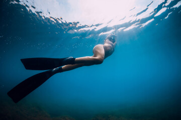Fototapeta na wymiar Sporty woman freediver with fins glides underwater in blue sea.