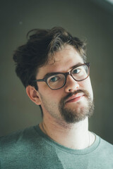 Obraz premium a handsome young man with a thick beard and glasses is illuminated on one side by a soft light. fashionable beard, happy. reflection in the mirror. irritation after shaving. very serious