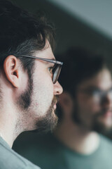 Obraz premium a handsome young man with a thick beard and glasses is illuminated on one side by a soft light. fashionable beard, happy. reflection in the mirror. irritation after shaving. shaves three times