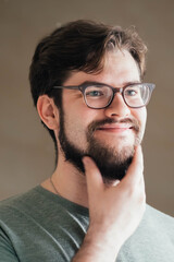 Obraz premium a handsome young man with a thick beard and glasses is illuminated on one side by a soft light. fashionable beard, satisfied