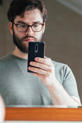 a handsome young man with a thick beard and glasses is holding a phone in his hands. takes a photo. read the news