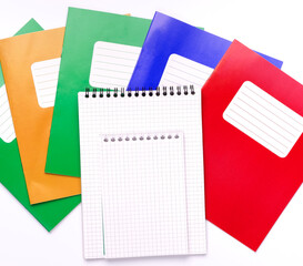 Colorful school exercise books and open page of note sheet on white background.