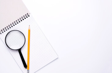 Blank white open notepad and magnifying glass on copy space background.