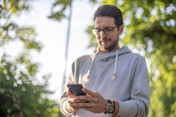 Smart looking man texting message on smartphone in park, back light