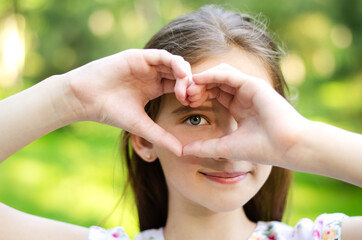 Smiling little girl holding hands near her eye with heart shape - 360481686
