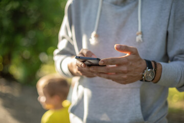 Man texting message on smartphone in park, back light