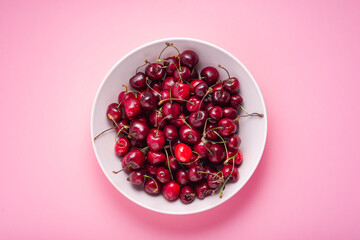 Fresh cherries in a bowl on a pink background, top view