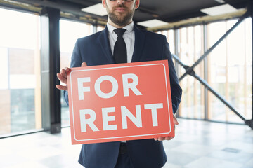 Close-up of realtor in suit holding placard in his hands while standing at modern office he...