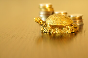Metal turtle on a gold background. Next to it is a stack of coins. Symbol of wealth and prosperity. Financial stability.