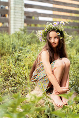 a girl with long hair with a wreath of flowers on her head is sitting on a stone