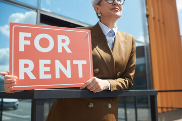 Close-up of real estate agent with placard For Rent standing outdoors