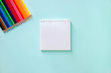 Horizontal minimalistic close-up flat lay composition with Clear sheet note book and colour pencils on a light blue background.  Back to school, college, education concept. Art supplies idea.